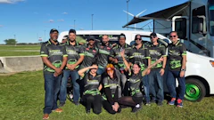 Team members in matching branded apparel pose together outdoors in front of an RV at a sporting event