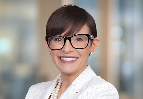 Professional headshot of a smiling woman wearing glasses and a white pinstriped blazer