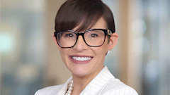 Professional headshot of a smiling woman wearing glasses and a white pinstriped blazer