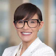 Professional headshot of a smiling woman wearing glasses and a white pinstriped blazer