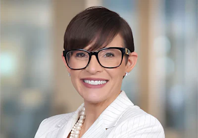 Professional headshot of a smiling woman wearing glasses and a white pinstriped blazer