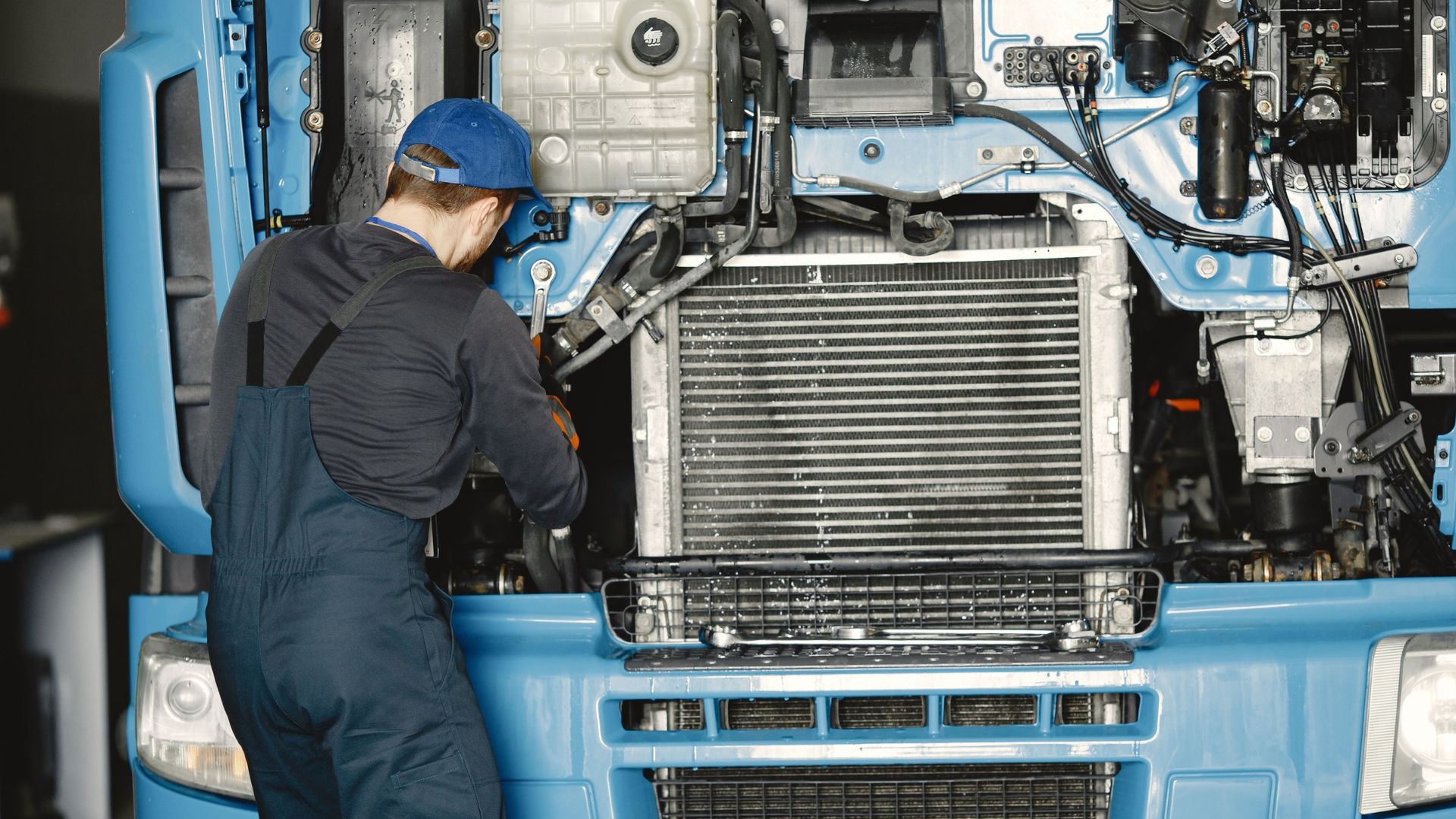 Mechanic in blue hard hat servicing truck engine with radiator and cooling system visible