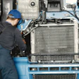 Mechanic in blue hard hat servicing truck engine with radiator and cooling system visible