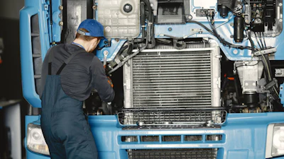 Mechanic in blue hard hat servicing truck engine with radiator and cooling system visible