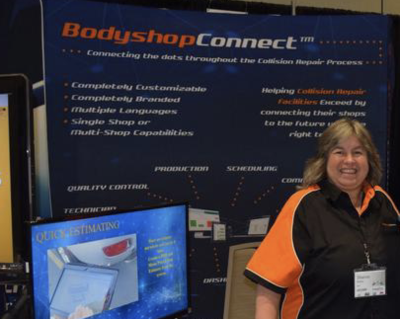 Woman presenting BodyshopConnect software solution at trade show booth with blue banner display