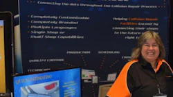 Woman presenting BodyshopConnect software solution at trade show booth with blue banner display