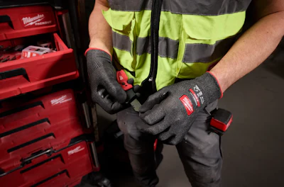 Worker in high-visibility vest wearing Milwaukee work gloves while holding tool storage case