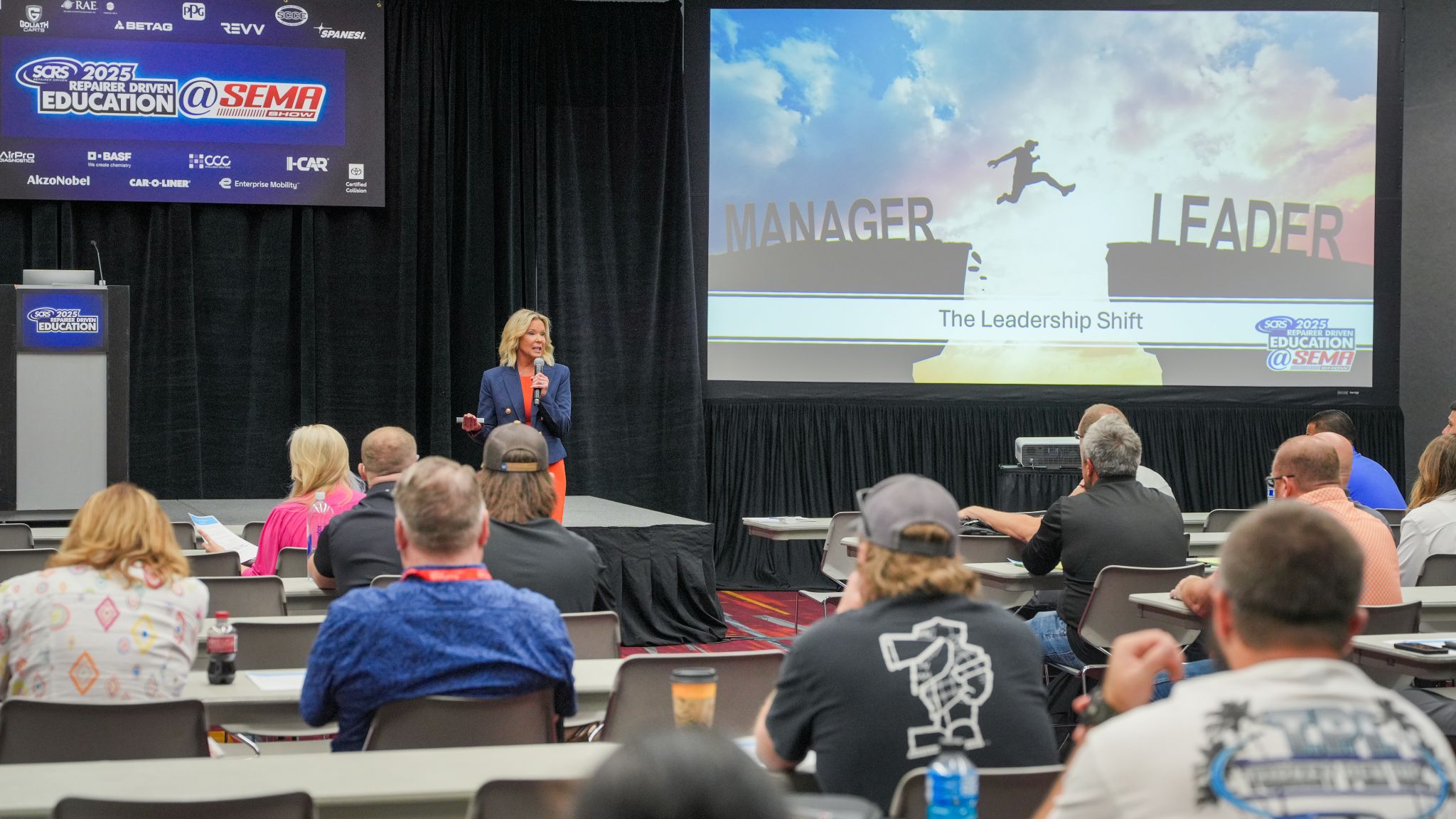 Professional speaker presenting 'The Leadership Shift' at SEMA education conference with audience seated at tables.