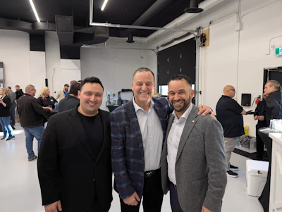 Three men smiling at a corporate event in a modern venue with attendees in the background
