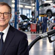 Professional man in business suit and glasses at automotive service center with vehicles and mechanics in background