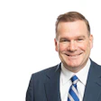 Professional headshot of a smiling man in business attire with blue striped tie