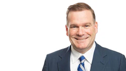 Professional headshot of a smiling man in business attire with blue striped tie