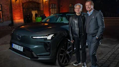 Two men in business casual attire pose beside a teal Renault electric vehicle outside a brick building at night
