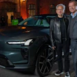Two men in business casual attire pose beside a teal Renault electric vehicle outside a brick building at night