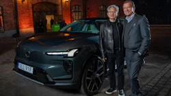 Two men in business casual attire pose beside a teal Renault electric vehicle outside a brick building at night