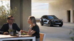 Two professionals discuss business while a sleek black Mazda SUV is displayed in a modern architectural space with floor-to-ceiling windows.