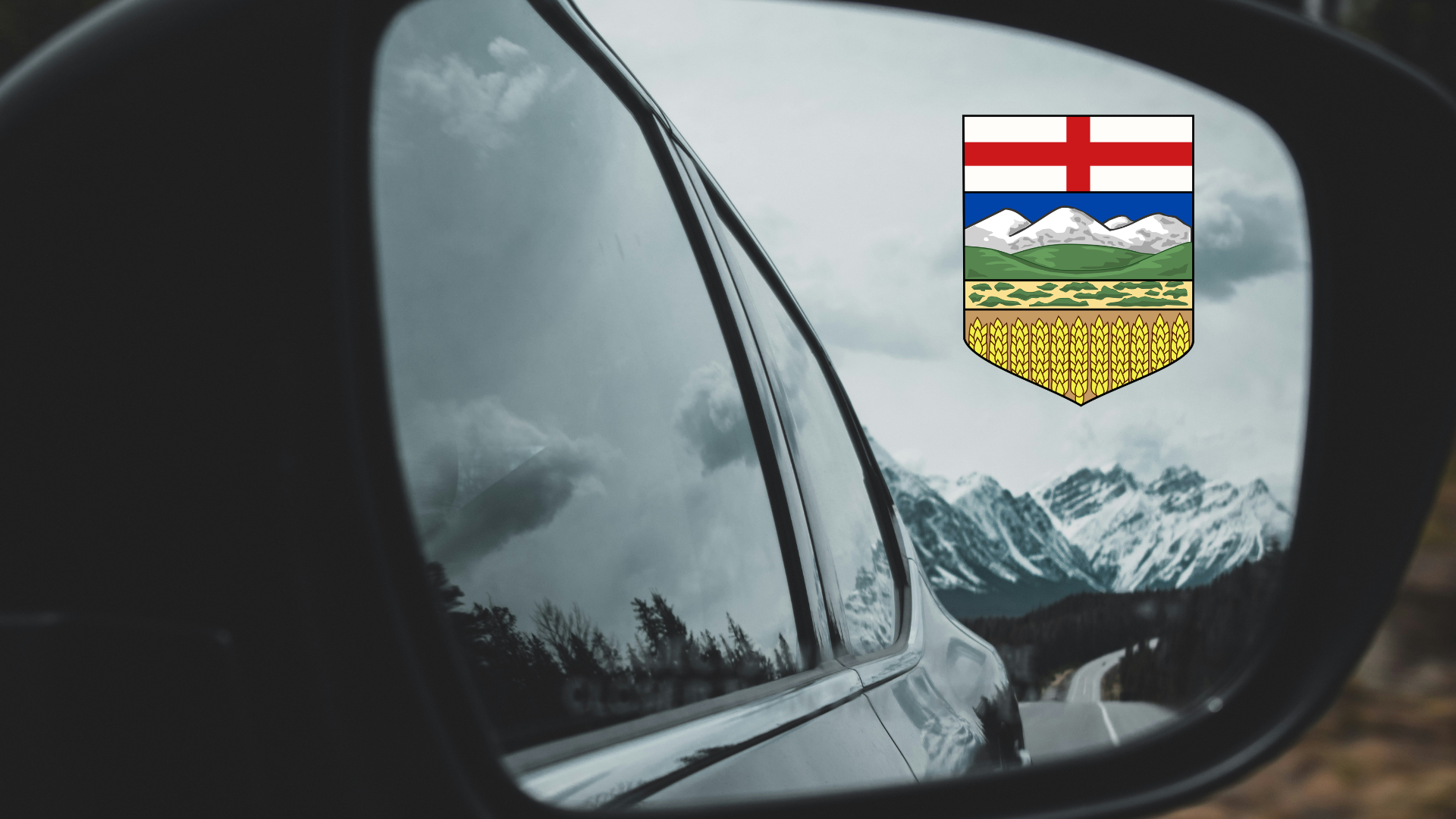 Alberta provincial shield reflected in car side mirror with snowy mountain landscape