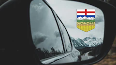Alberta provincial shield reflected in car side mirror with snowy mountain landscape