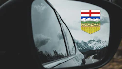 Alberta provincial shield reflected in car side mirror with snowy mountain landscape