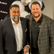 Two men smiling at corporate event with AECX branded backdrop and red carpet