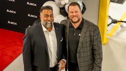 Two men smiling at corporate event with AECX branded backdrop and red carpet