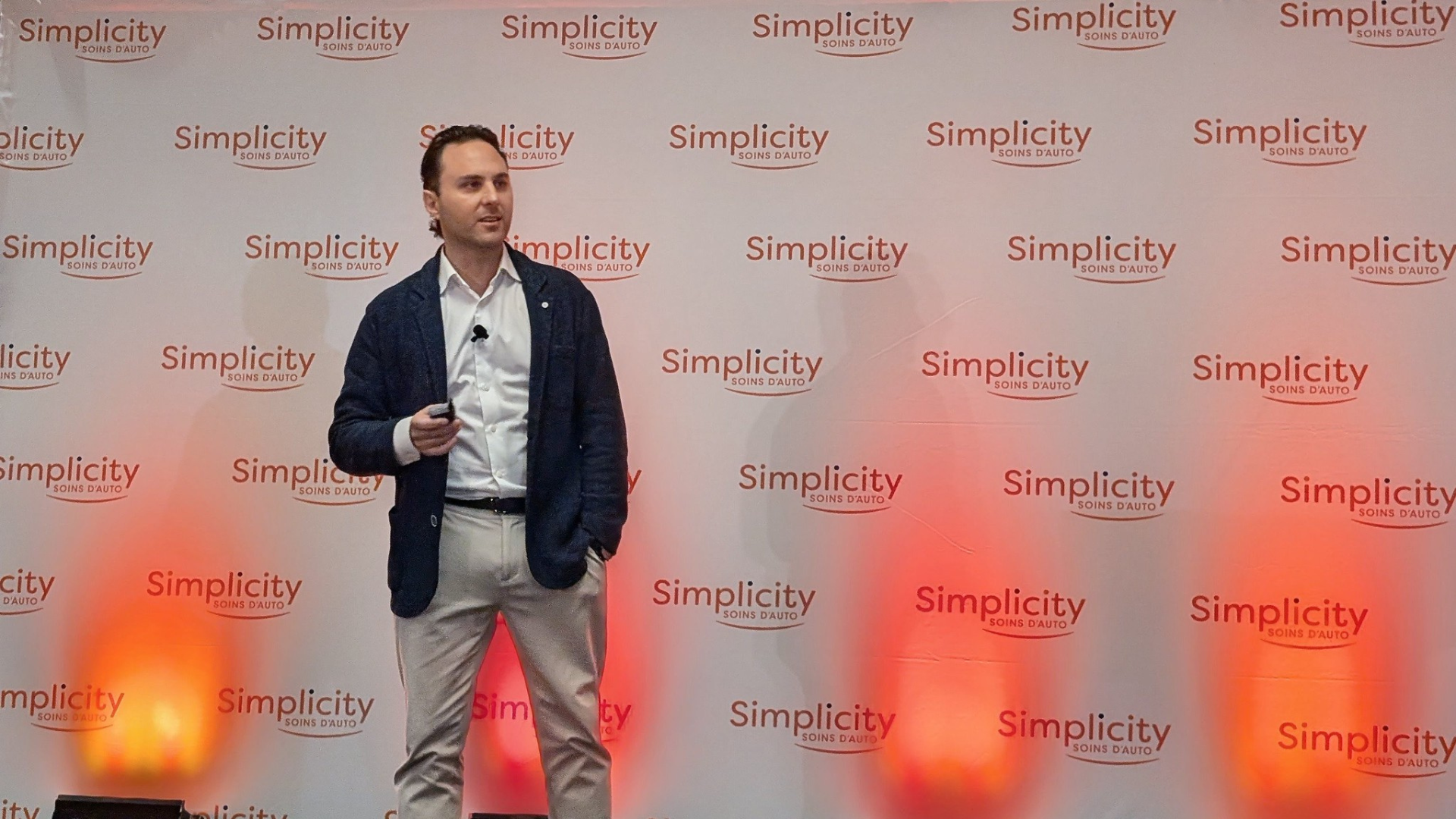 Professional speaker presenting at Simplicity event with branded backdrop