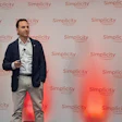 Professional speaker presenting at Simplicity event with branded backdrop