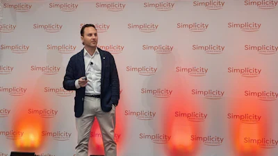 Professional speaker presenting at Simplicity event with branded backdrop