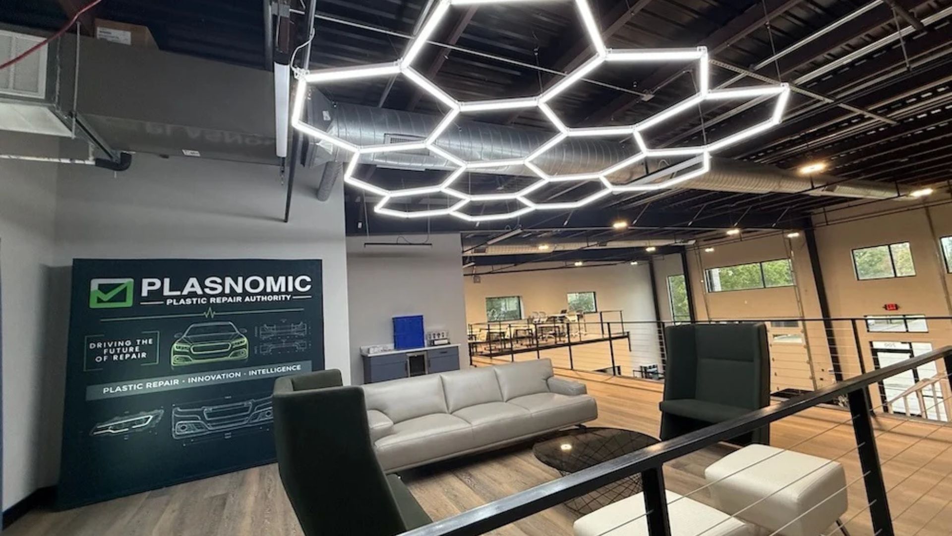 Modern office showroom with Plasnomic plastic repair branding on dark wall, hexagonal ceiling lights, and contemporary furniture