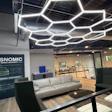 Modern office showroom with Plasnomic plastic repair branding on dark wall, hexagonal ceiling lights, and contemporary furniture