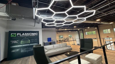 Modern office showroom with Plasnomic plastic repair branding on dark wall, hexagonal ceiling lights, and contemporary furniture