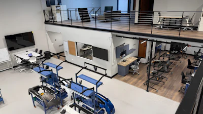 Modern two-story office space with mezzanine featuring blue workstations, white cabinetry, and wooden flooring