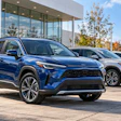 Blue Toyota SUV displayed at dealership lot with additional vehicles and modern showroom building in background