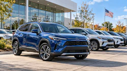 Blue Toyota SUV displayed at dealership lot with additional vehicles and modern showroom building in background