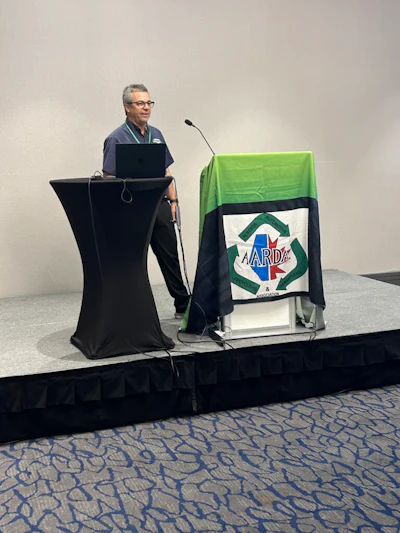 Professional man presenting at podium with ARDA recycling logo banner during conference presentation