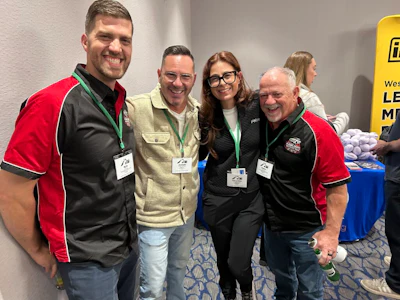 Five professionals wearing ID badges smile together at a conference or networking event indoors.
