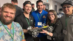 Group of five people at a tech event holding a robotic device with white wheels and wearing conference badges