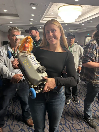 Woman holding orange and gray submarine toy at indoor event with attendees in background