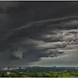 Dramatic storm clouds gathering over a residential cityscape with dark skies and rain shafts