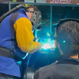 Welder performing welding demonstration with bright arc light and blue and yellow protective equipment at trade show or educational event